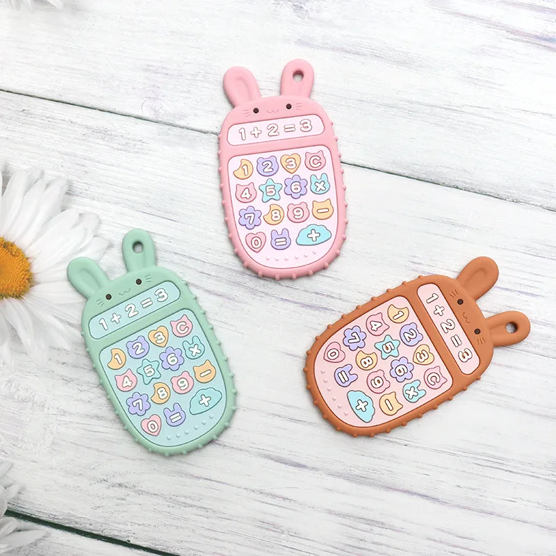 Three colorful Tipi Tipi Tap bunny calculator silicone teethers on a light wooden surface with a daisy flower.