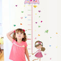 Child measuring their height against a decorative Tipi Tipi Tap Girl's Umbrella Height Chart wall decal with colorful elements.