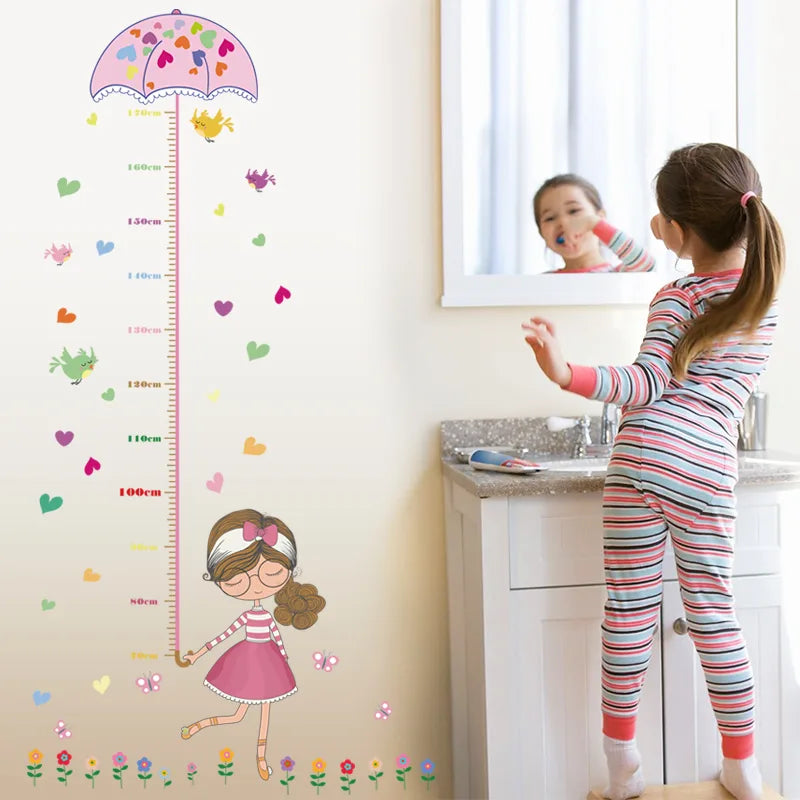 Child standing on a step stool in front of mirror next to a Tipi Tipi Tap Girl's Umbrella Height Chart wall decal.