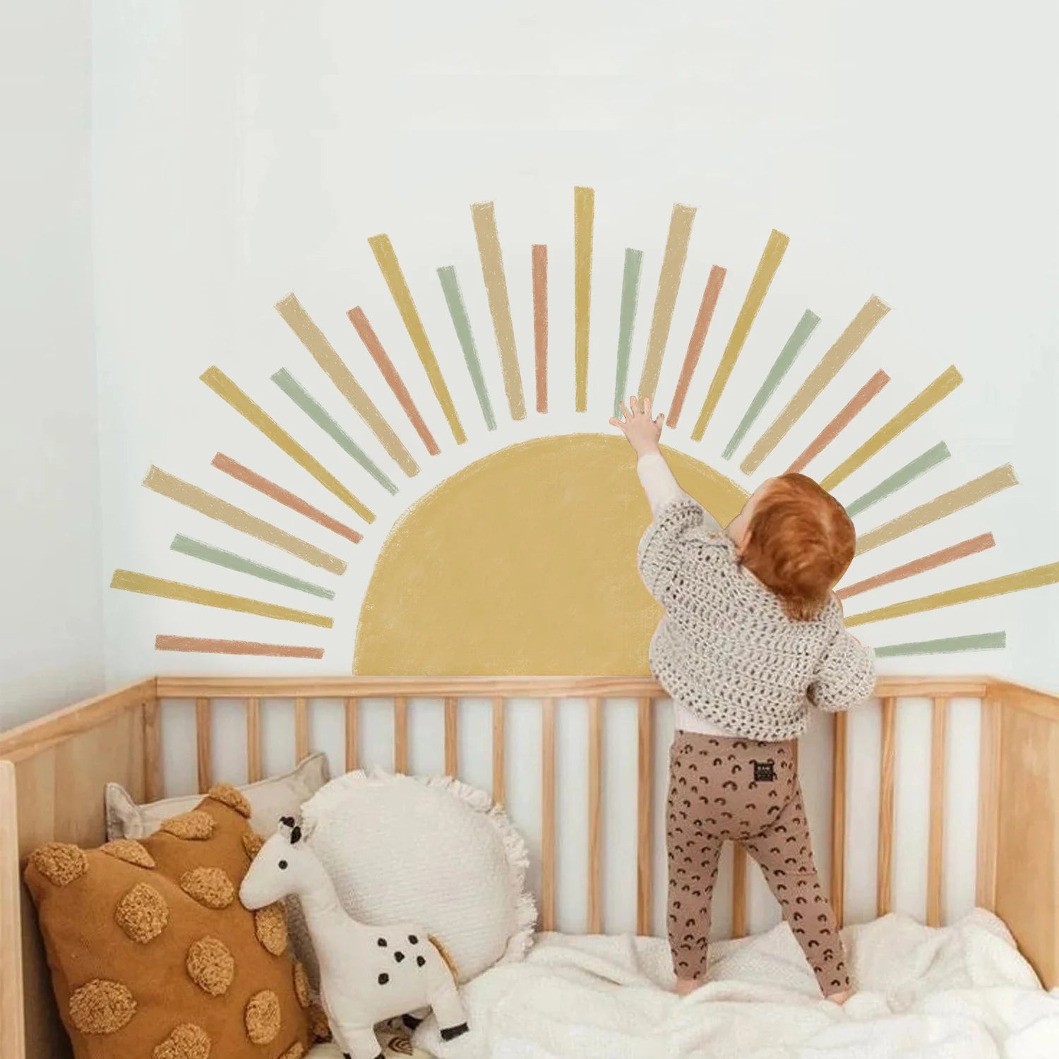 Child standing on a bed with Tipi Tipi Tap Sunburst Half Sun wall decal on wall in a nursery.