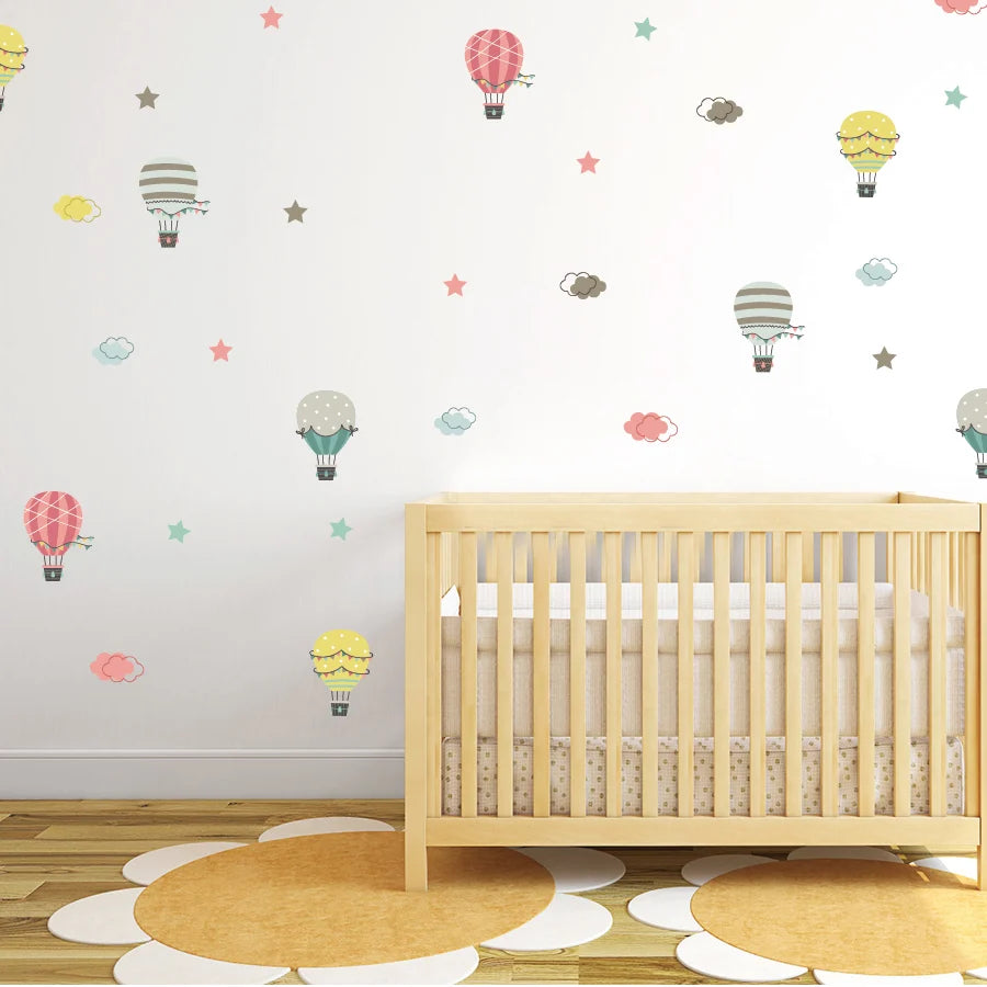 Wooden crib in a room with colorful Tipi Tipi Tap Hot Air Balloon & Cloud wall decals on a white wall.