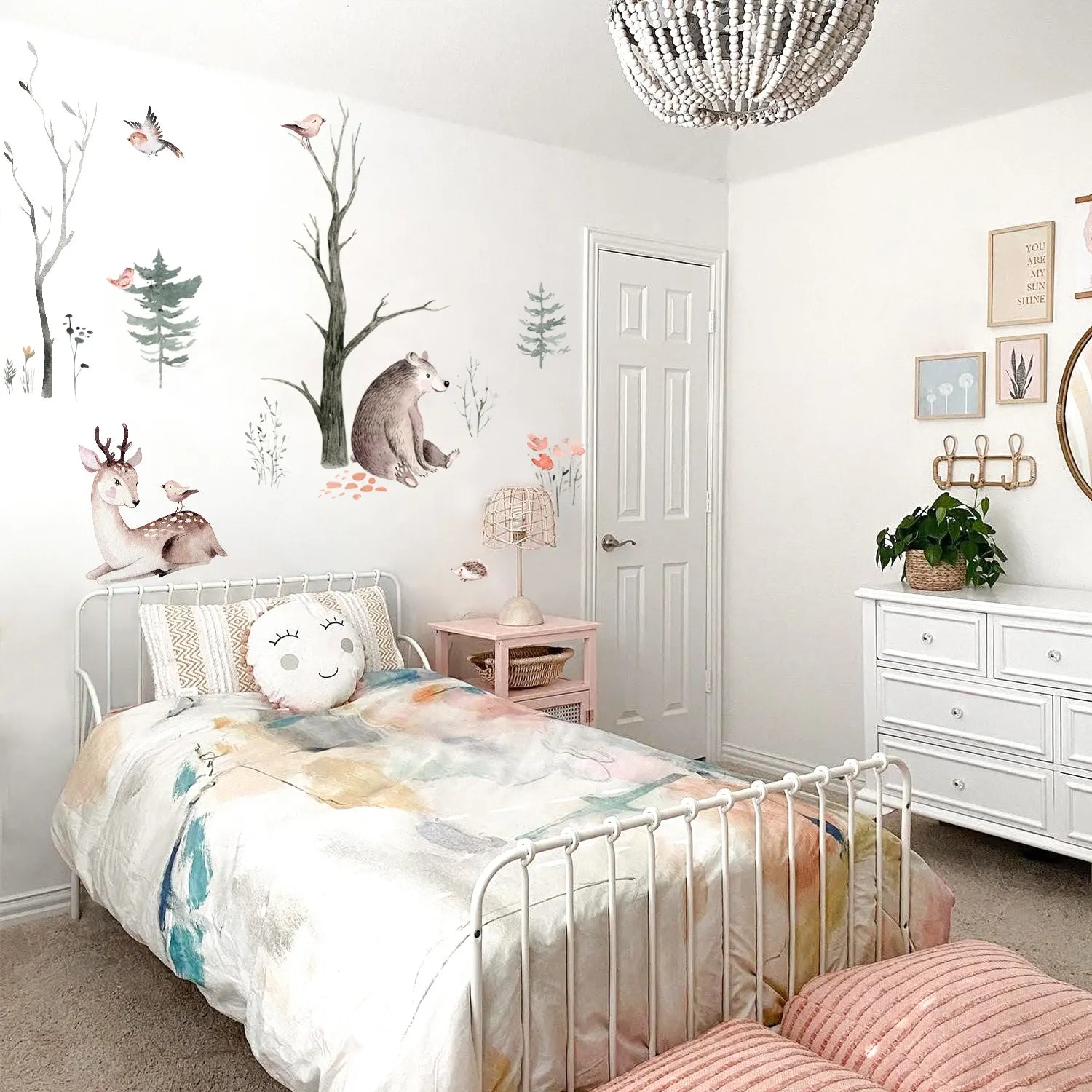Children's bedroom with a white bed, floral bedding, and wall decals of trees and animals.