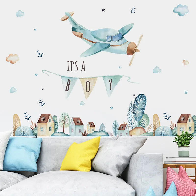 Decorative wall sticker with airplane and 'It's a Boy' banner over a sofa with colorful cushions.