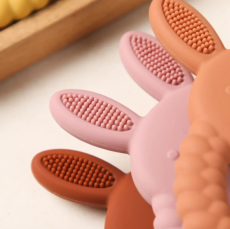 Pink, beige and brown Tipi Tipi Tap Rabbit Silicone Baby Teethers on a light background