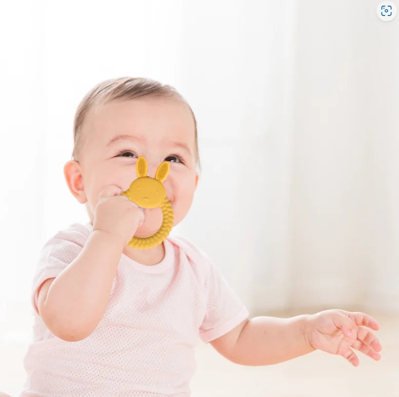 Baby holding a yellow Tipi Tipi Tap Rabbit Silicone Baby Teether against a white background