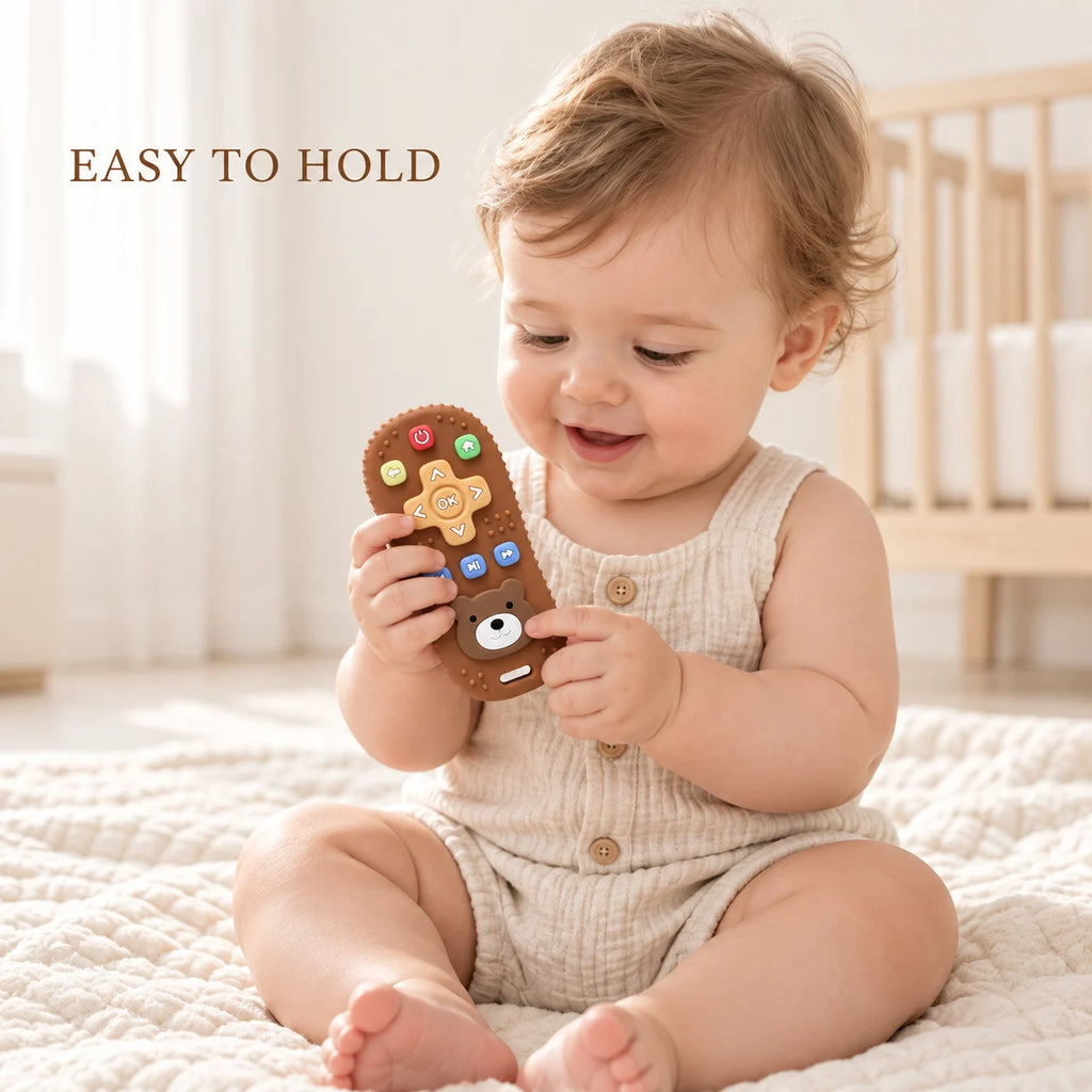 A baby sitting on a cream quilted blanket in a bright nursery, holding a brown Tipi Tipi Tap Silicone Baby Remote Teether with colorful buttons. The text 'EASY TO HOLD' is visible in the top left corner.