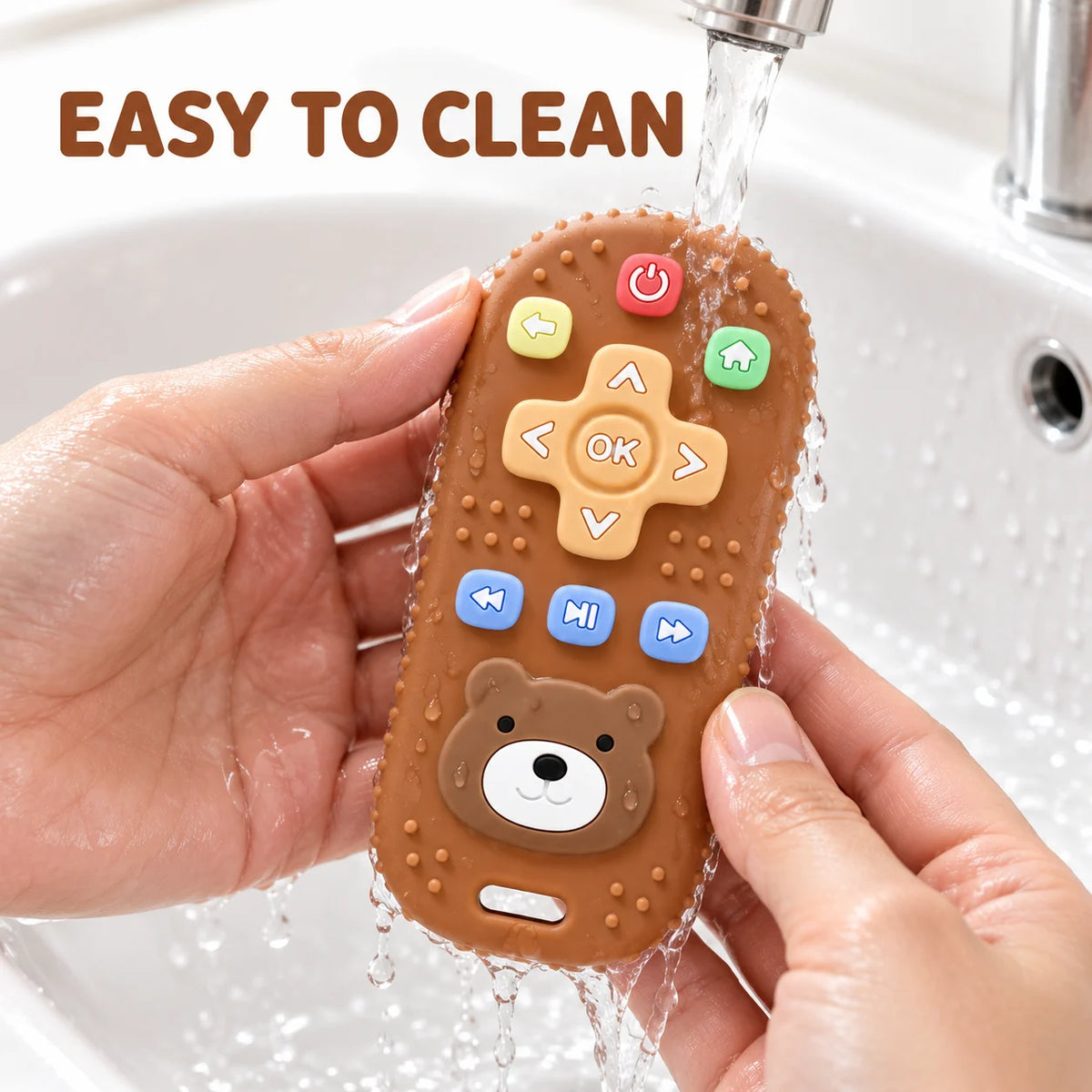 A person holds a brown Tipi Tipi Tap Silicone Baby Remote Teether under running water in a sink, with the text 'EASY TO CLEAN' at the top. The teether has colorful button details and a bear face design.