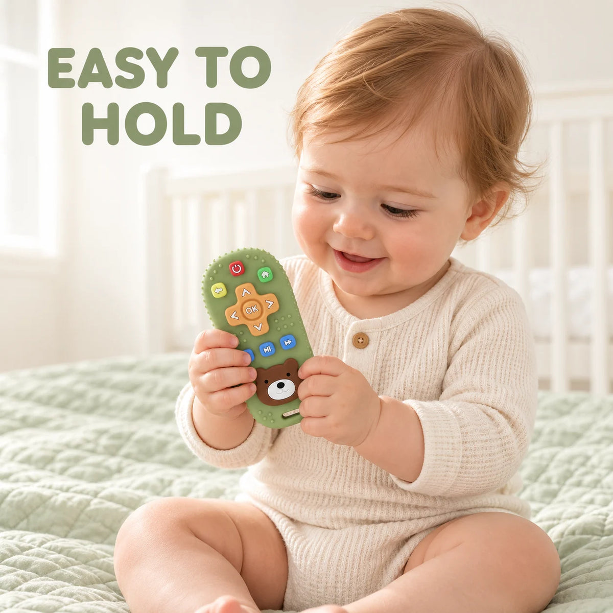 A baby sitting on a light green quilted bed holds a green Tipi Tipi Tap Silicone Baby Remote Teether with colorful buttons and a bear face. Large text in the upper left reads 'EASY TO HOLD'.