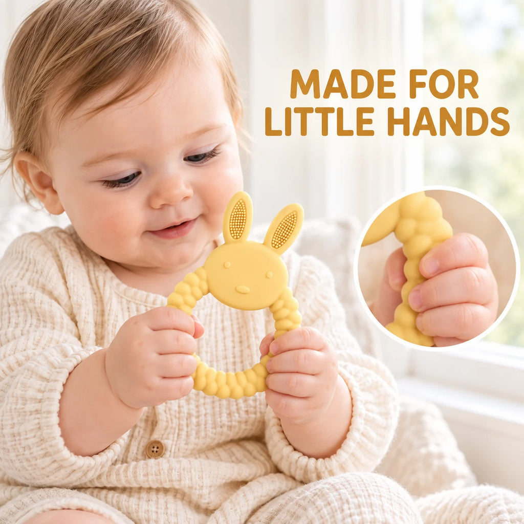 A baby in a cream knit outfit holds a yellow Tipi Tipi Tap Rabbit Silicone Baby Teether. The image includes the text 'MADE FOR LITTLE HANDS' and a circular inset showing a close-up of a hand squeezing the textured yellow teether.