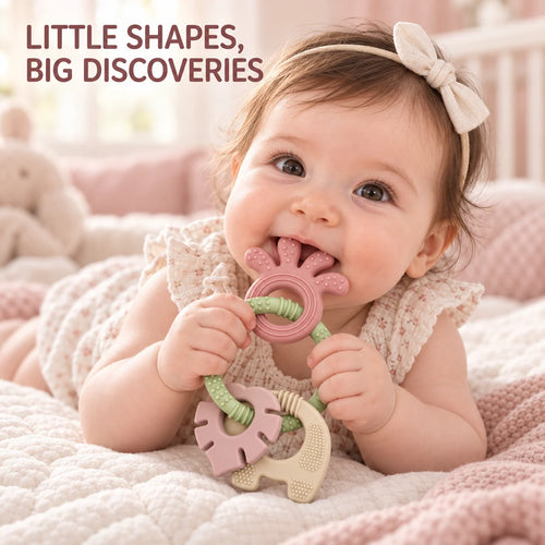 A baby lying on a quilted blanket and interacting with a Tipi Tipi Tap 4-in-1 Silicone Baby Teether Ring Set. The toy has a pink bunny-shaped teether with a green rope and a beige elephant-shaped teether.