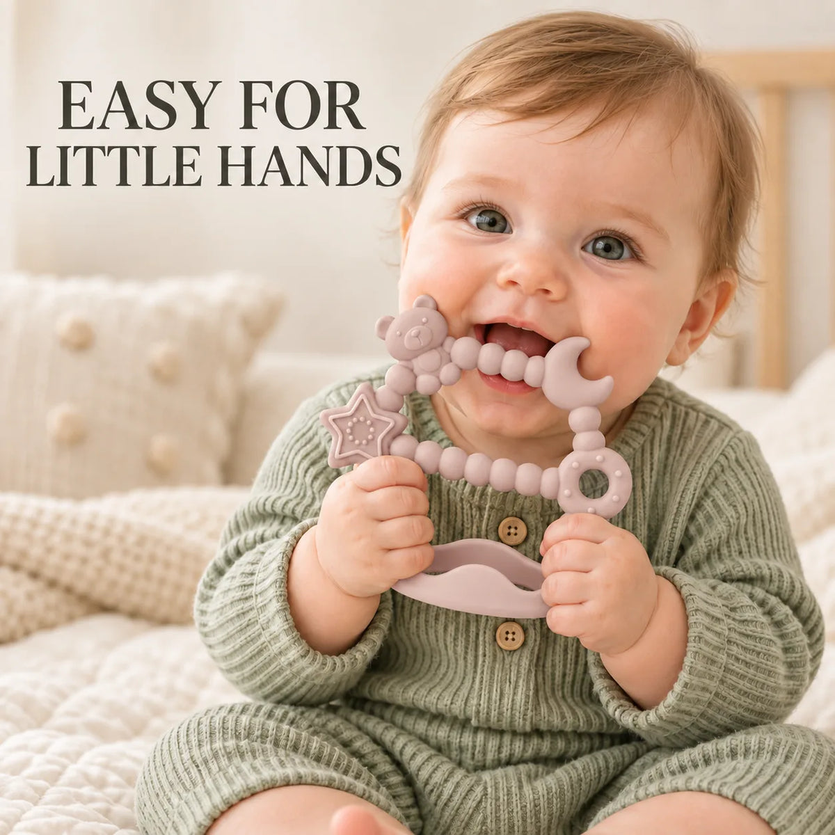 A baby wearing a sage green knit romper sits on a cream quilted bed and holds a pastel pink Tipi Tipi Tap Silicone Baby Wrist Teether (Moon & Star) with a bear, moon, star. Large text in the upper left reads 'EASY FOR LITTLE HANDS'.