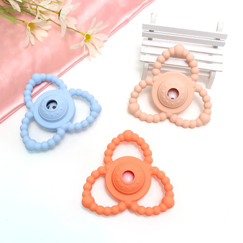 Three Tipi Tipi Tap Triangular Rattle Teether in blue, peach, and orange colors on a white background with flowers.
