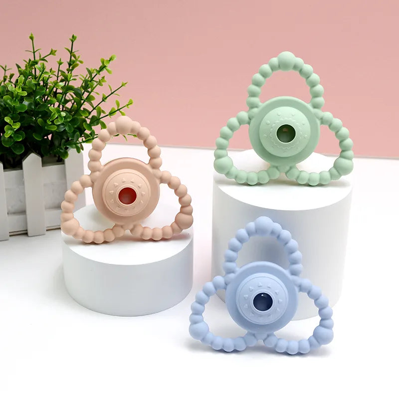 Three colorful Tipi Tipi Tap Triangular Rattle Teether on white cylindrical stands with a pink background.